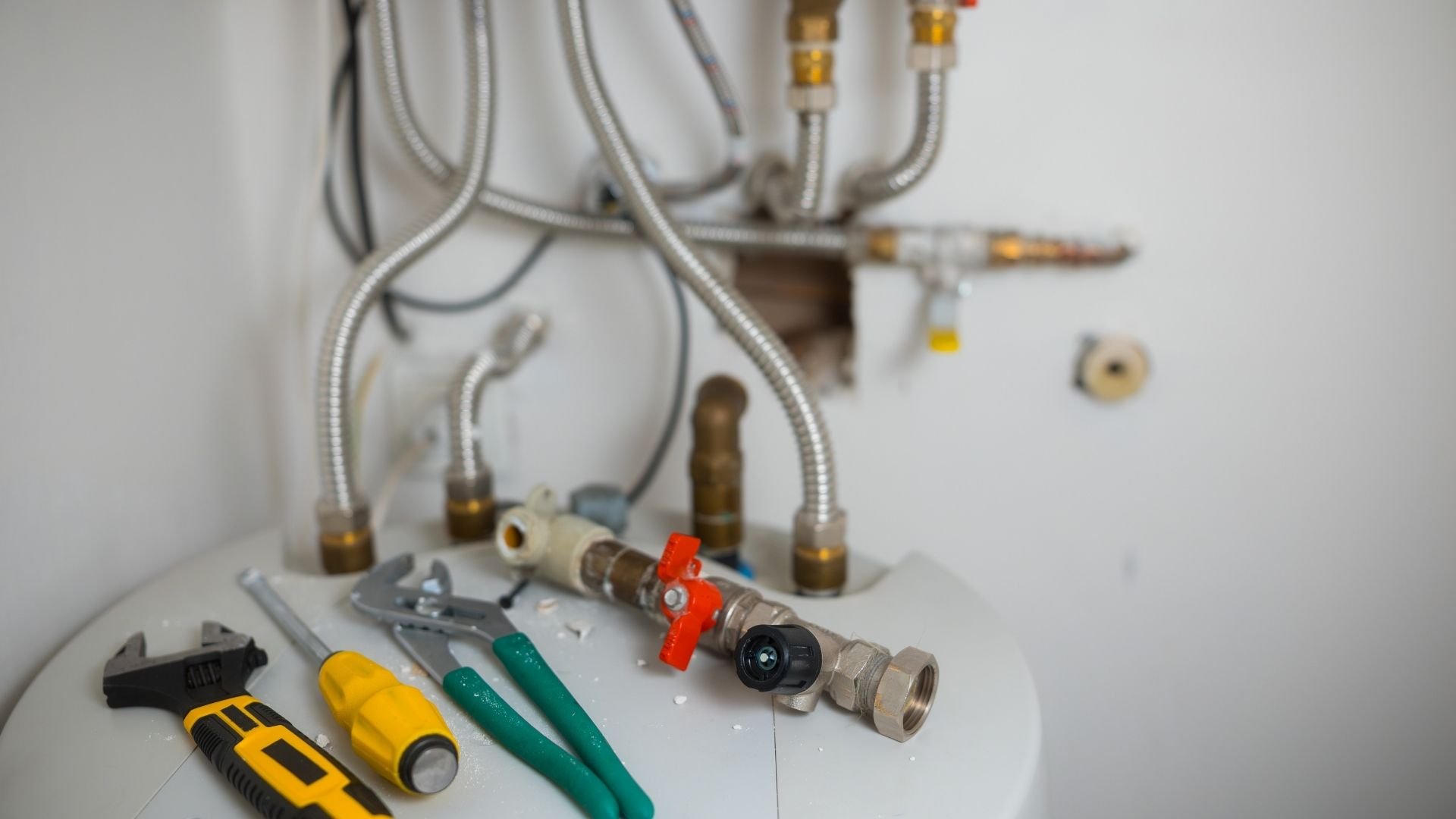 Plumbing tools and brass fittings with metal tubing and red valve handles on white surface