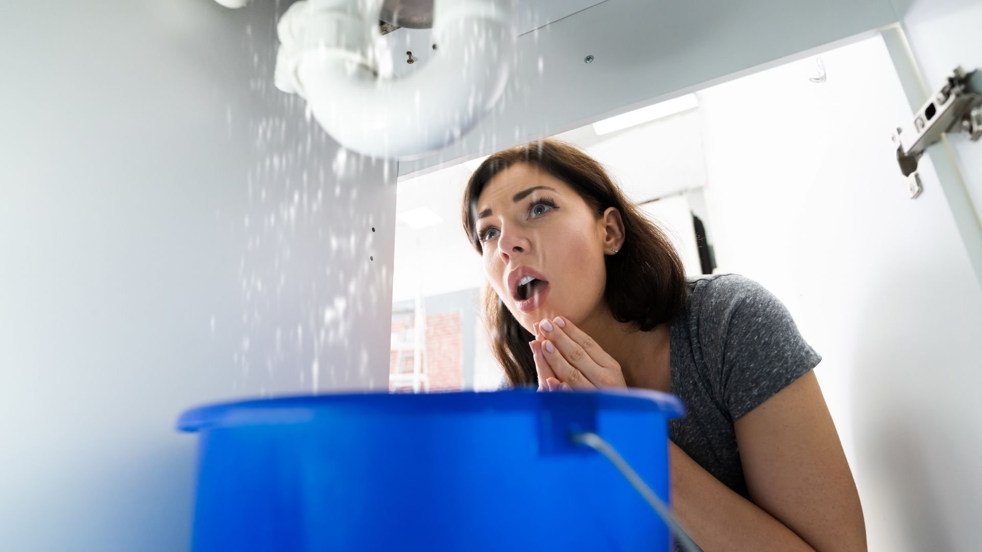 Woman looking shocked at leaking ceiling water with blue bucket below