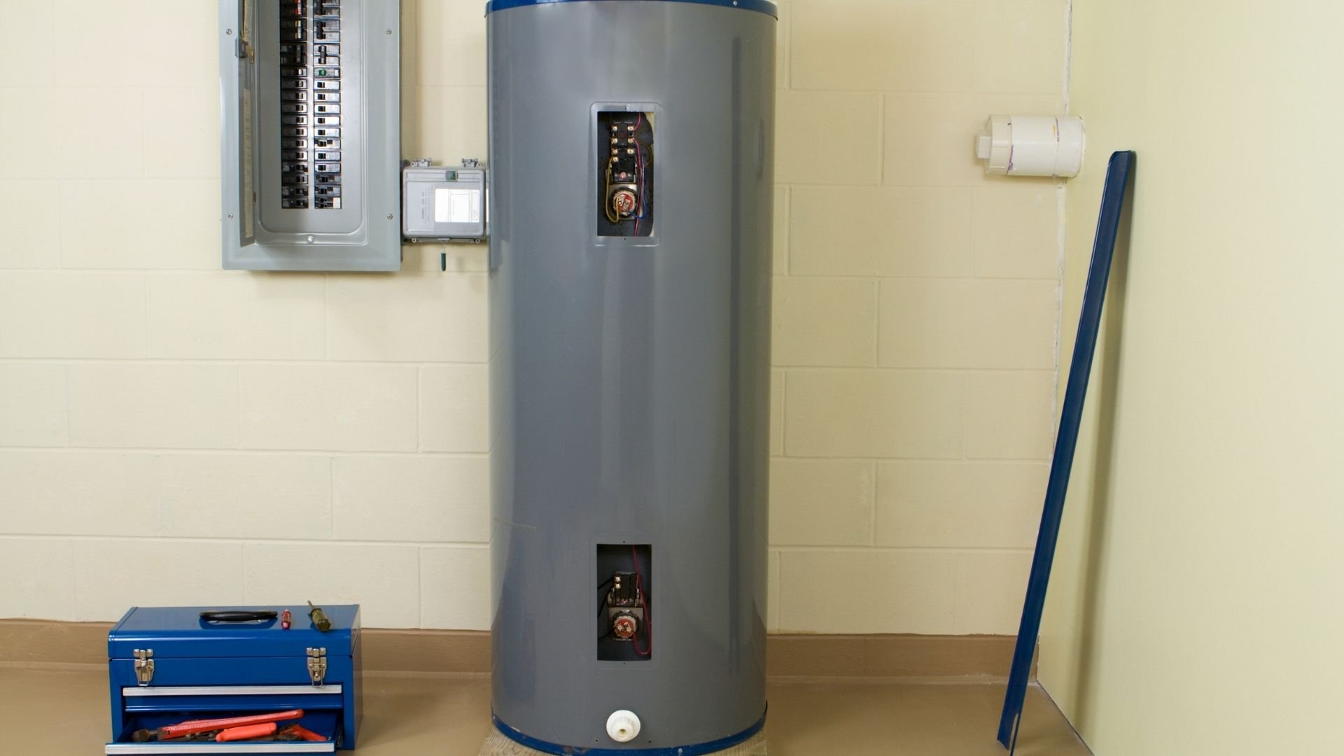Gray cylindrical water heater with blue trim next to electrical panel and tools.