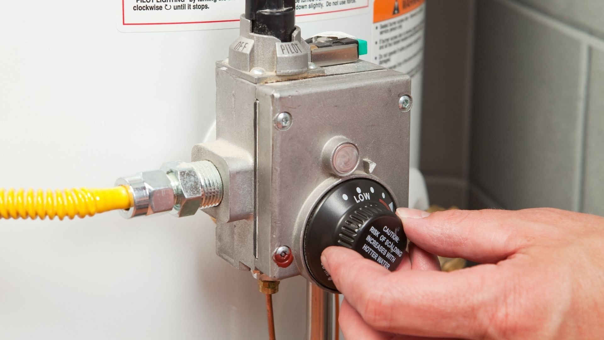 Hand adjusting pilot light dial on gas water heater control valve