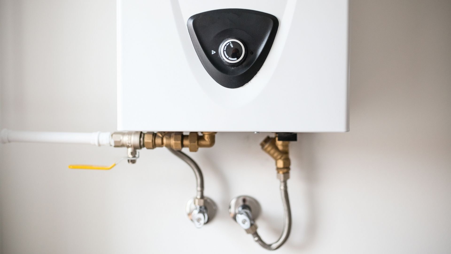 White tankless water heater mounted on wall with brass connections and control dial