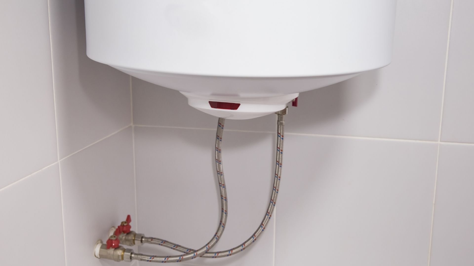 White wall-mounted sink with red valve and metal supply hoses in bathroom