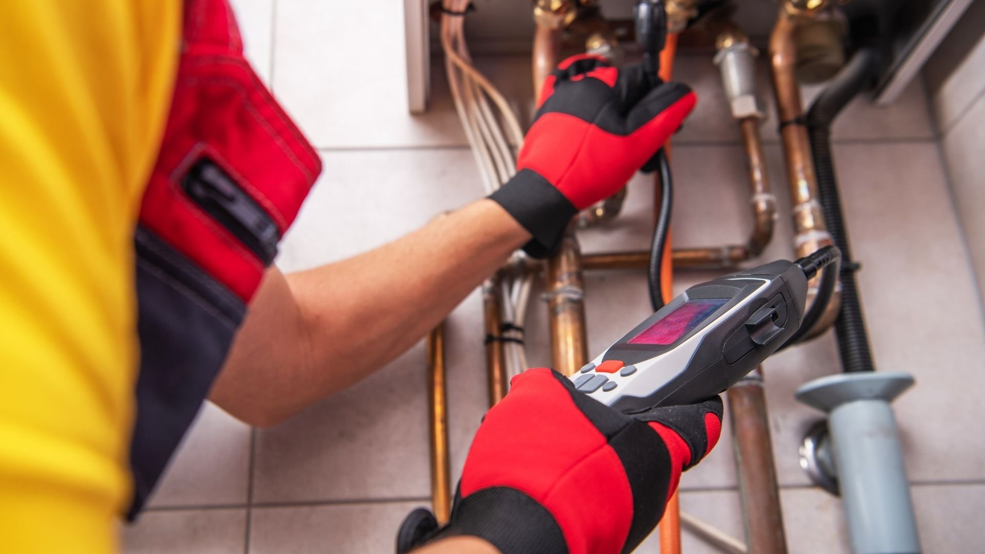 Technician in red and black gloves holding infrared thermal imaging device near electrical equipment