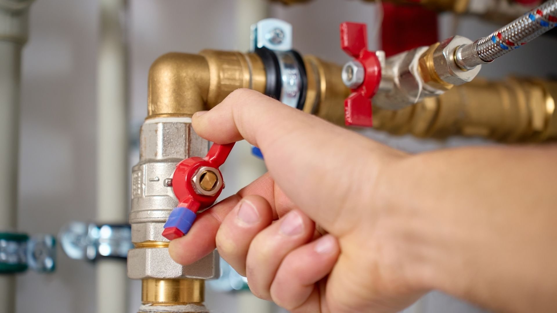 Hand turning red valve on brass water pipe plumbing fixture