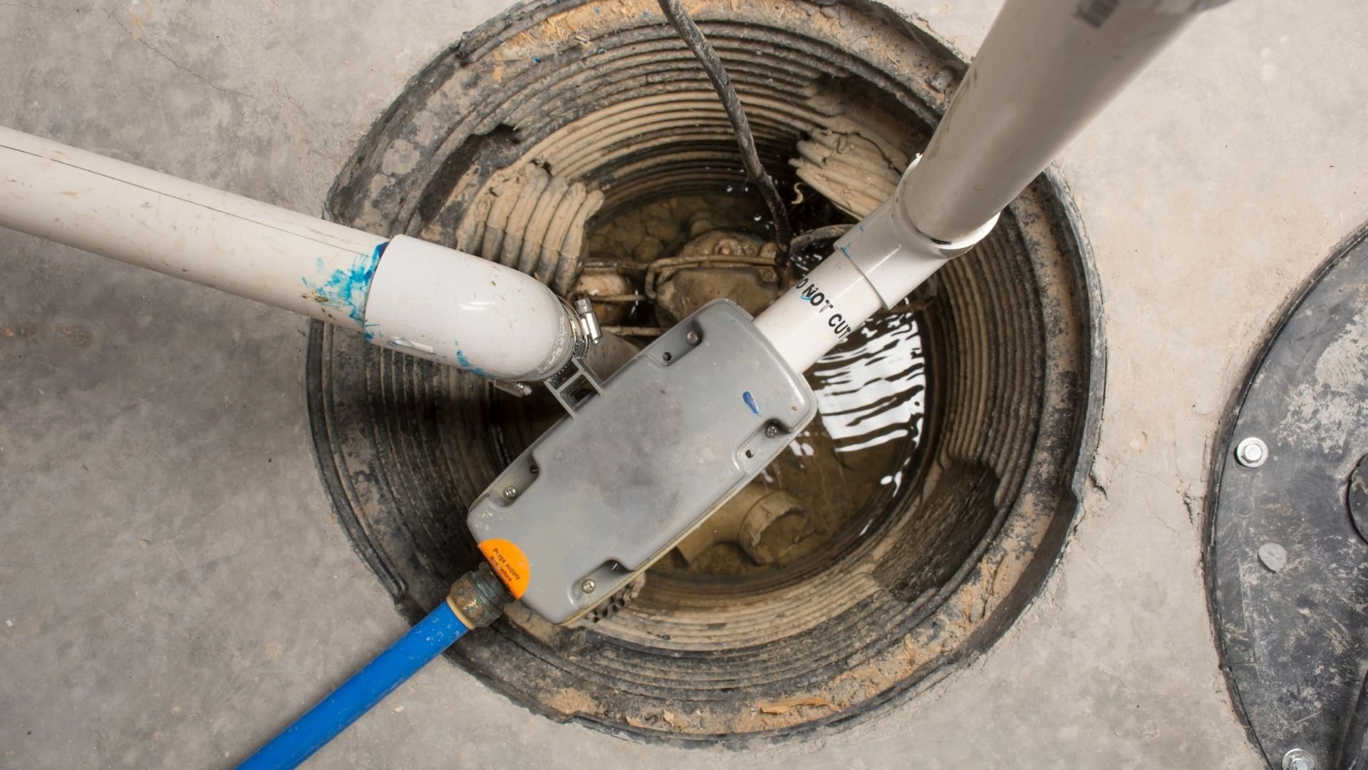 Submersible pump being lowered into open concrete manhole pipe underground