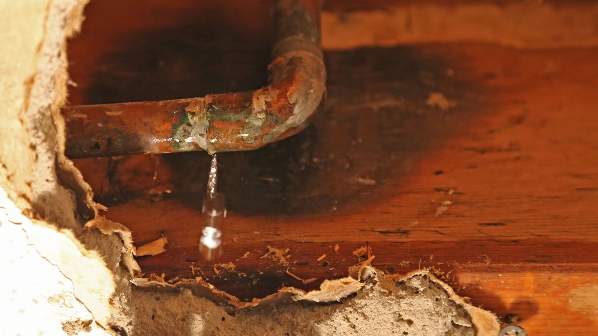 Rusty metal pipe with water droplet dripping onto reddish-brown surface