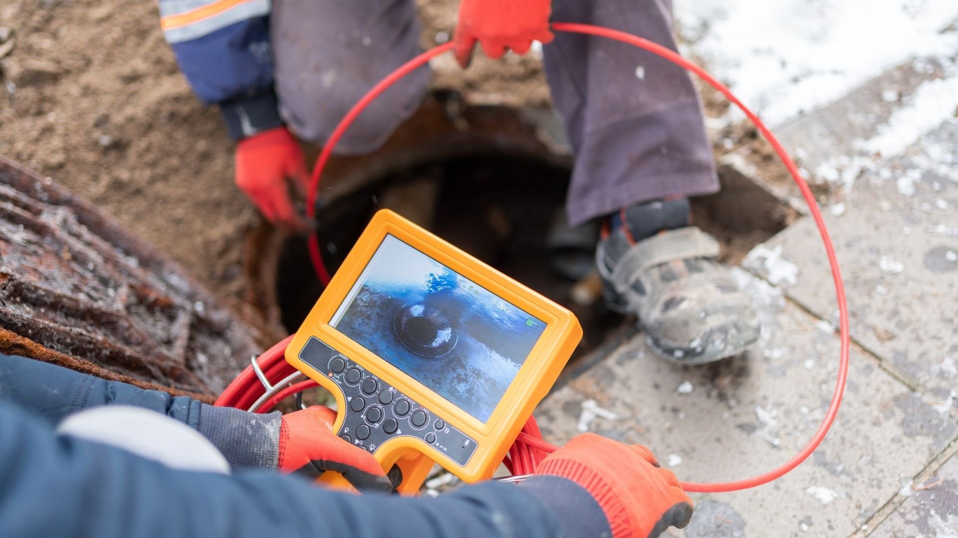 Technician holding yellow inspection camera displaying pipe interior on monitor during industrial inspection