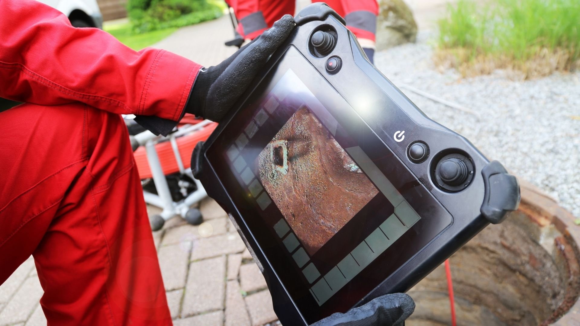 Person in red jacket holding thermal imaging camera displaying brick building exterior.