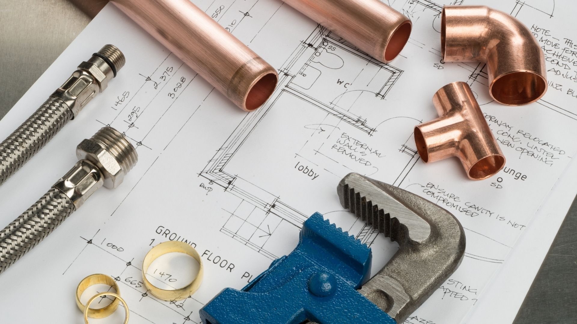 Plumbing tools and copper pipes on architectural blueprints and technical drawings