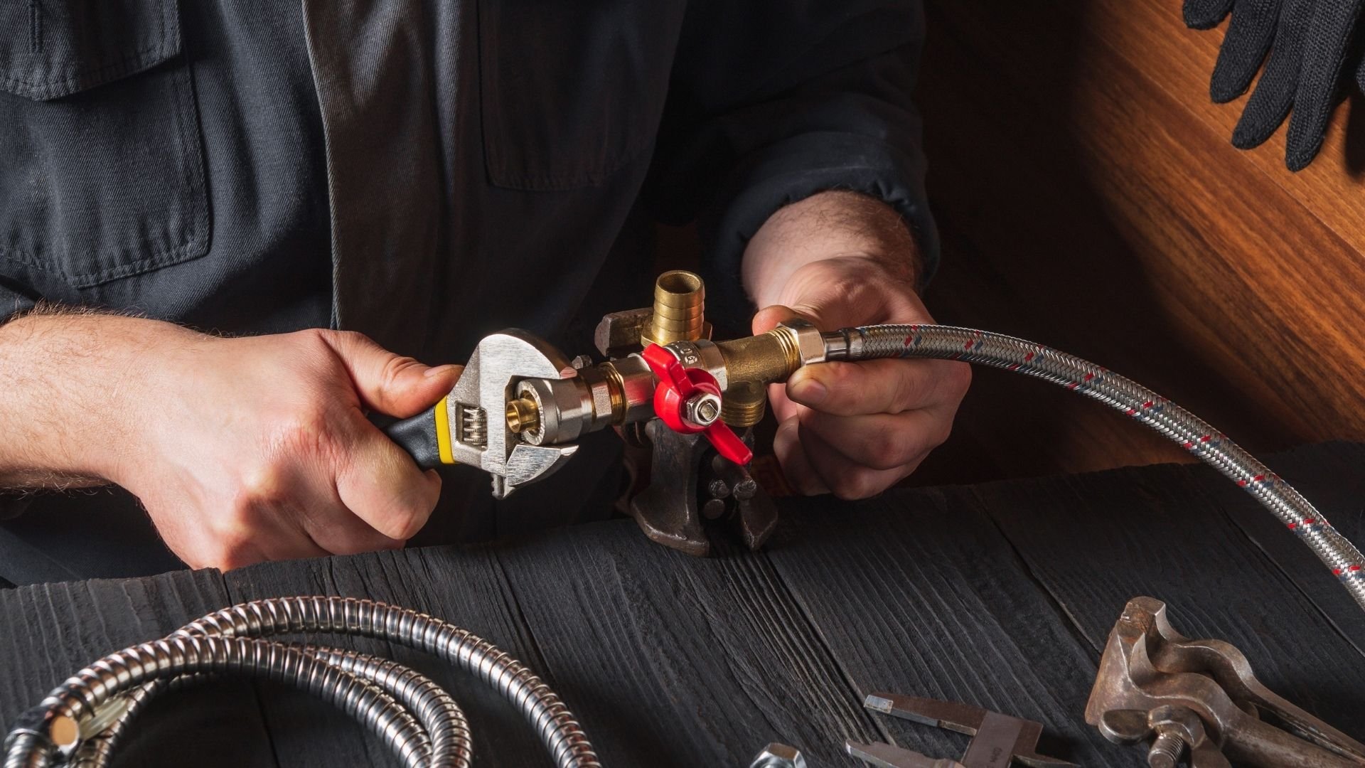 Plumber adjusting brass valve with wrench on metal flex hose pipe